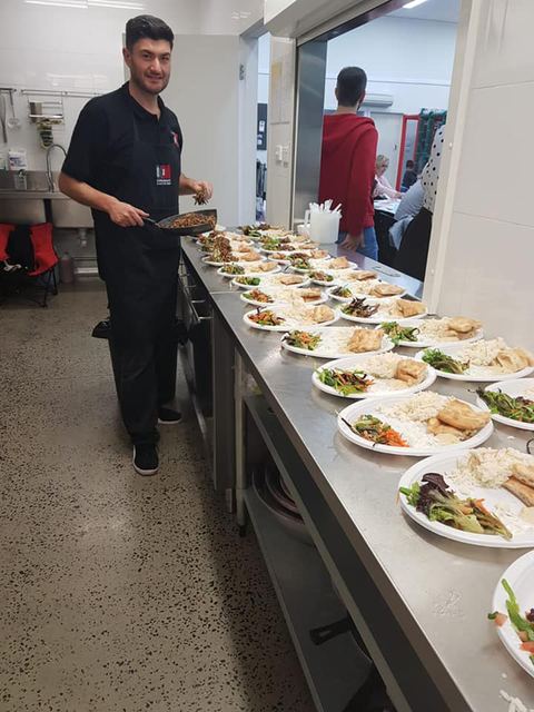 A cook at a long counter lined with plated wraps and salads